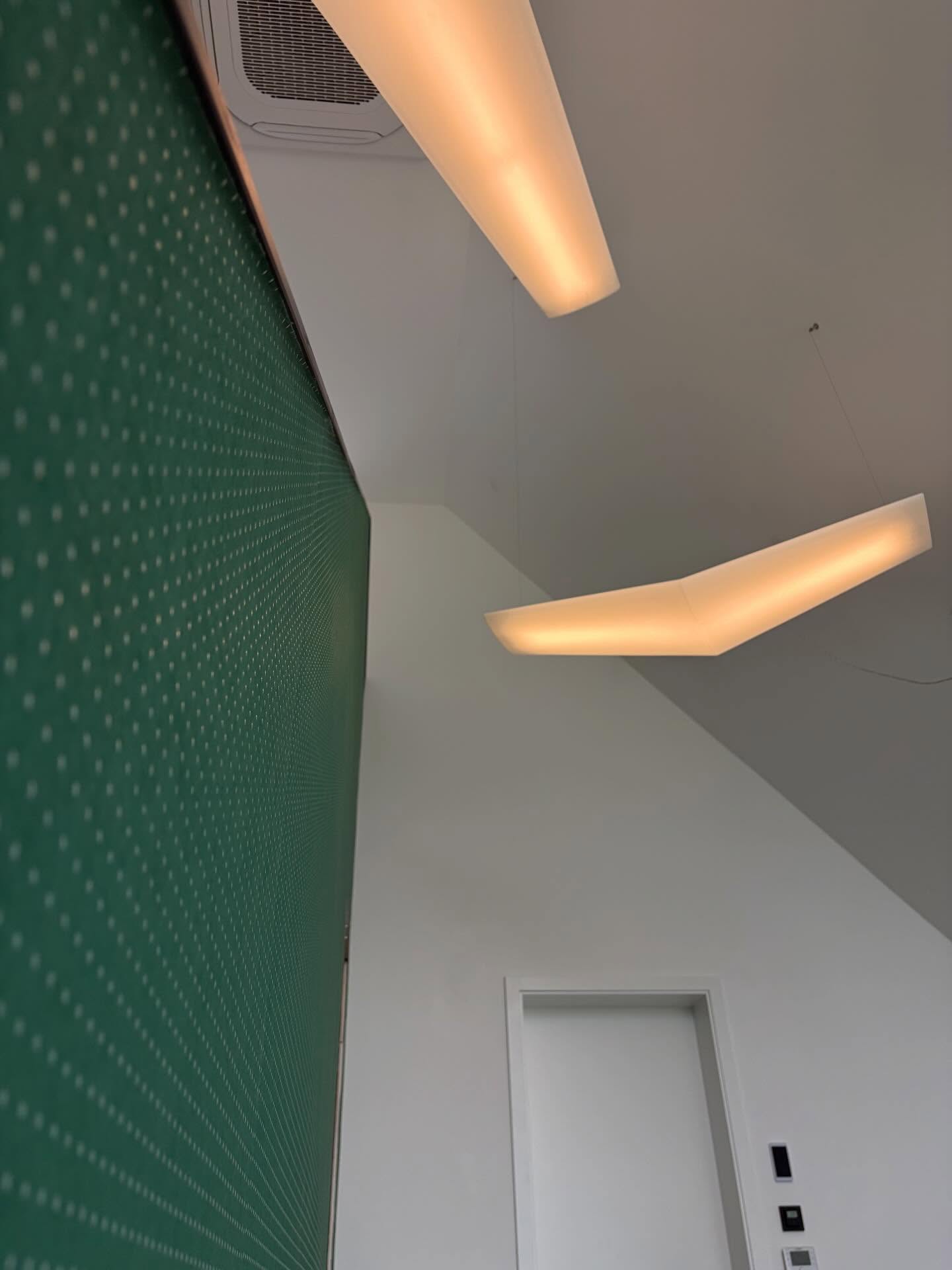 Grüne Wand mit Punktmuster von unten gesehen, darüber Lichtbänder an der Decke.
