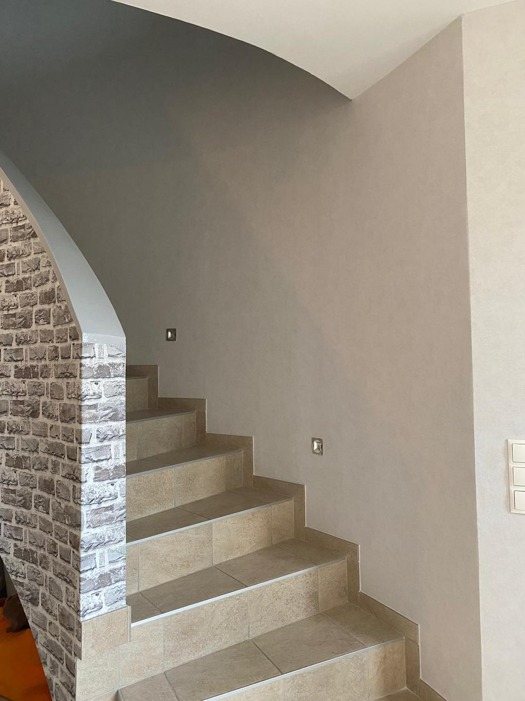 Treppenlauf mit der Brüstung in Steinoptik links und einer hellen Wand rechts.