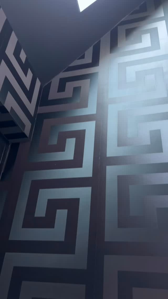 Schwarze Tapete mit silbernem Mäander-Ornament in einer Raumecke.