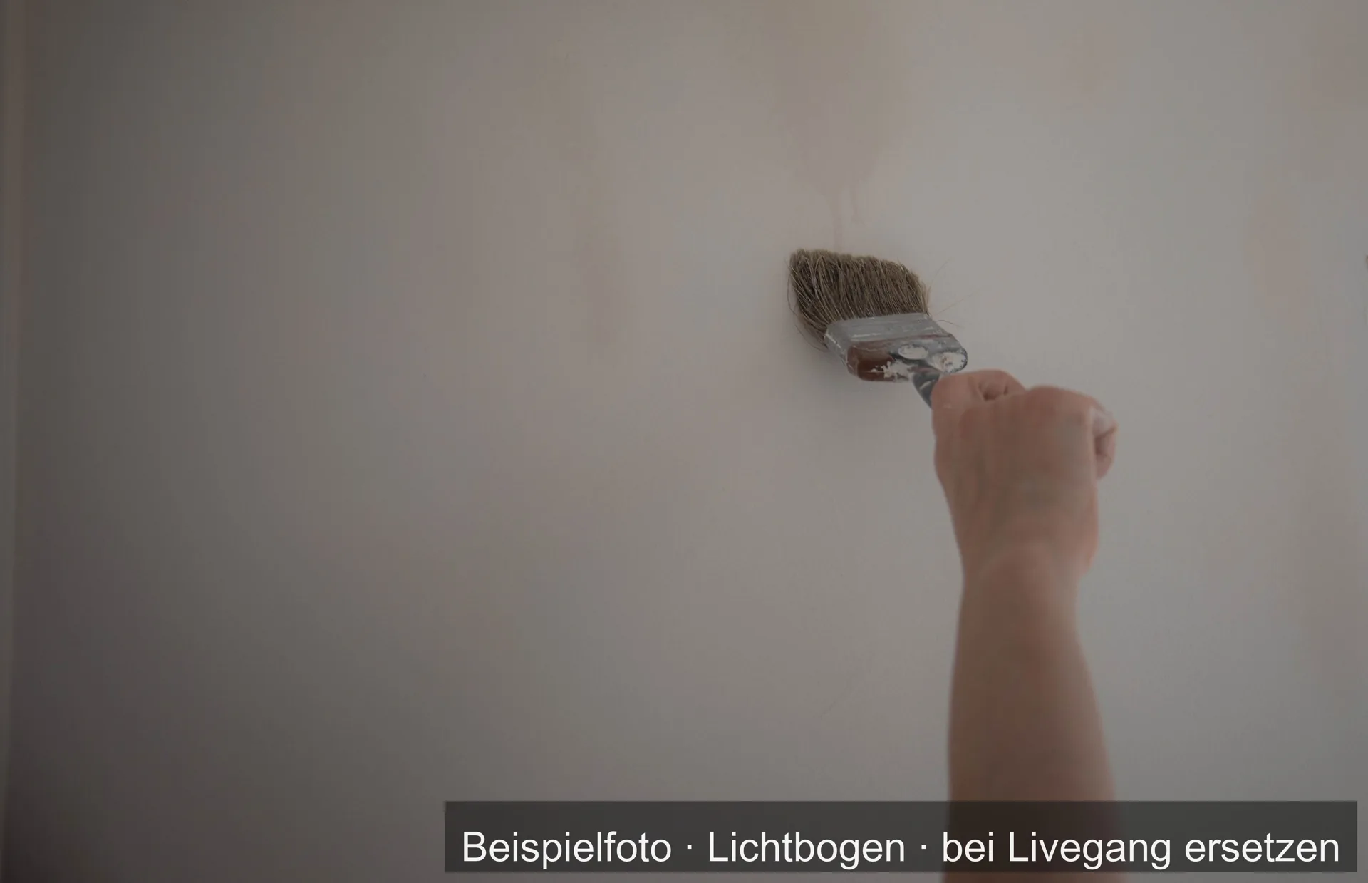 Eine Hand streicht mit dem Pinsel eine helle Wand.