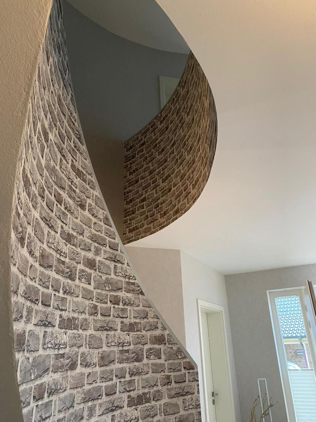 Dieselbe Treppe von unten, das Band in Steinoptik windet sich im Tageslicht nach oben.
