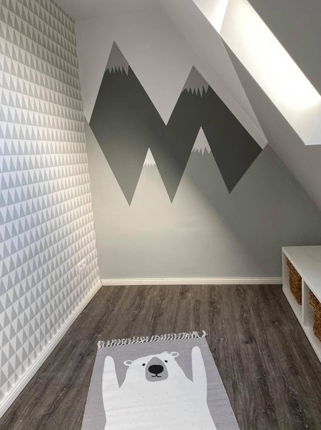 Kinderzimmer unter der Dachschräge mit grauer Bergsilhouette an der Stirnwand, links eine Tapete mit Dreiecksmuster, davor ein Eisbär-Teppich.