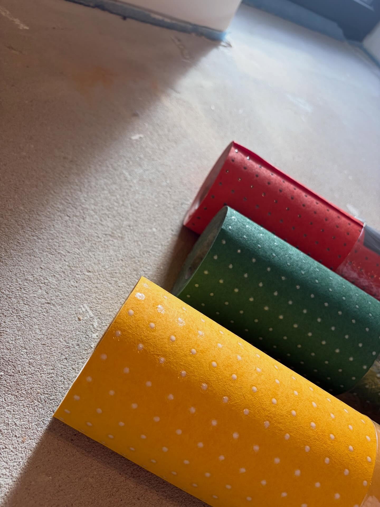 Tapetenrollen mit Punktmuster in Gelb, Grün und Rot liegen auf dem Boden.