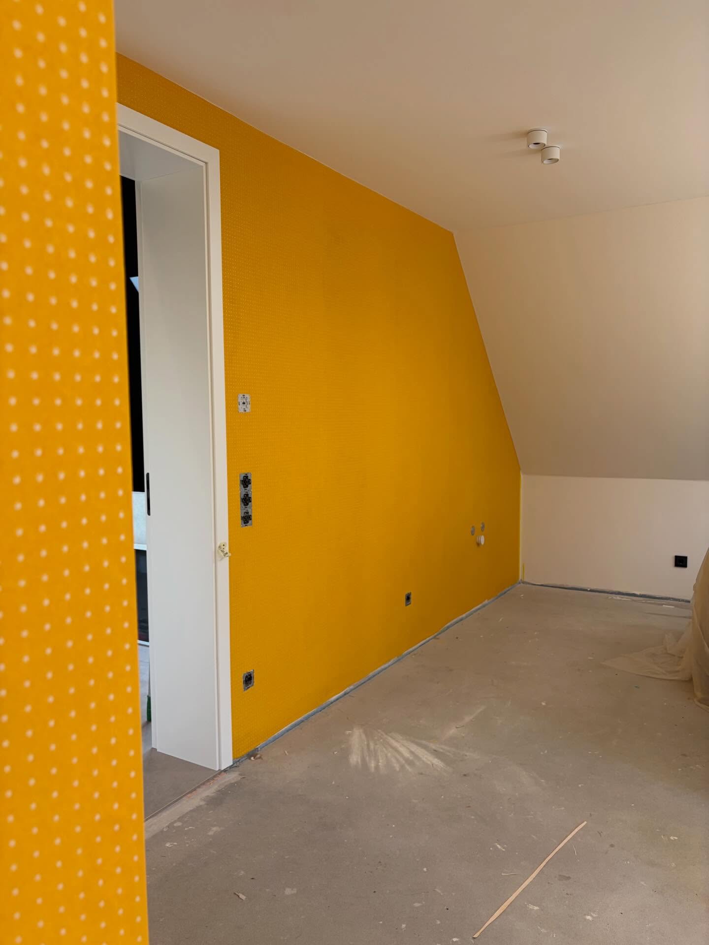 Gelb gestrichene Wand unter der Dachschräge, daneben eine Tapete mit gelben Punkten.