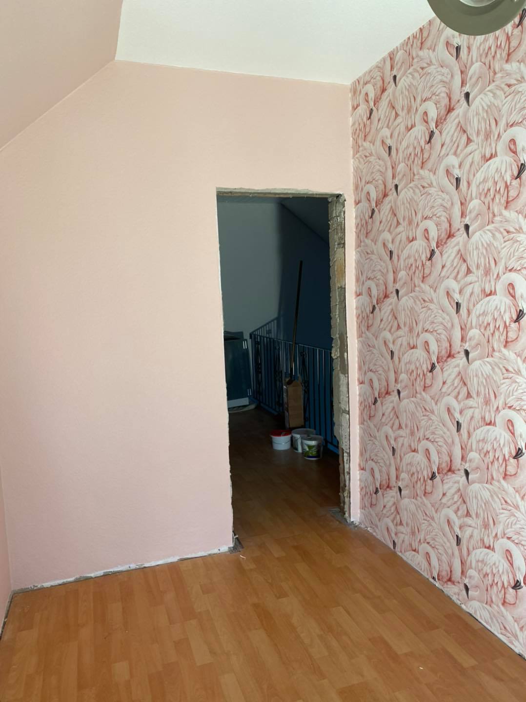 Durchgang mit Flamingo-Tapete neben einer rosé gestrichenen Wand, dahinter das Treppenhaus.