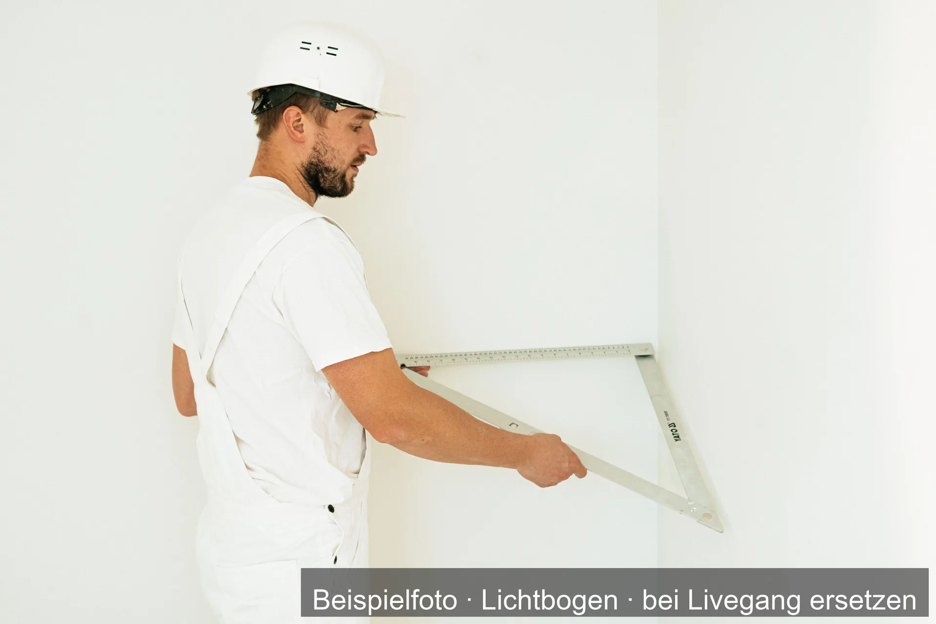 Maler in weißer Arbeitskleidung hält einen Winkel an eine weiße Wand.