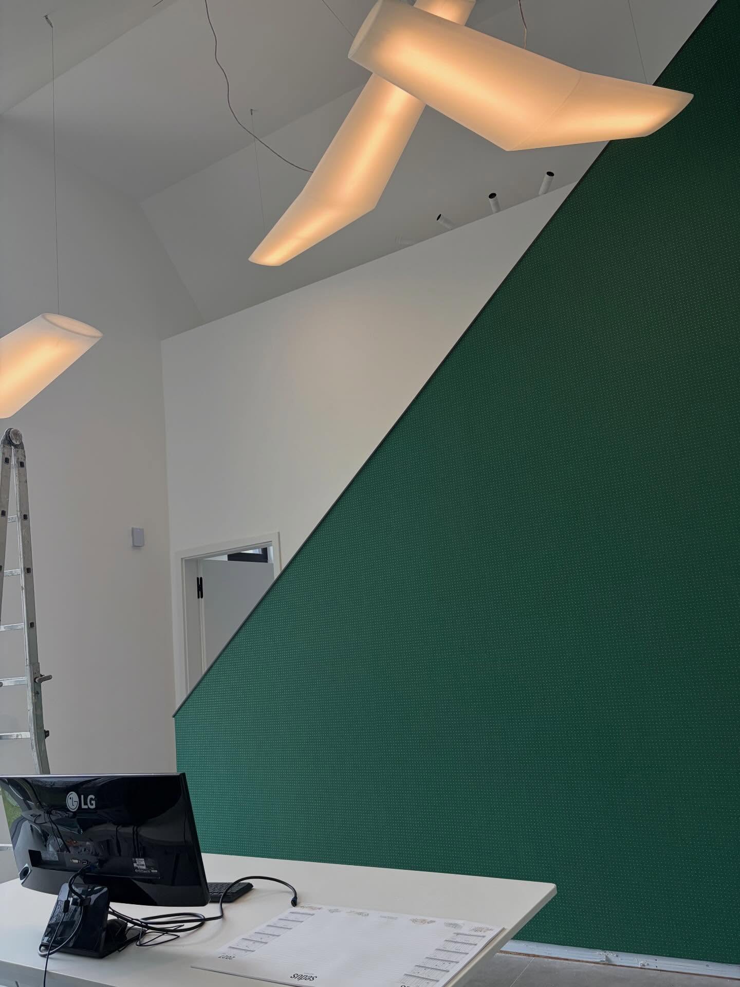 Raum mit Dachschräge und großer tannengrüner Wand mit feinem Punktmuster, darunter ein Schreibtisch mit Bildschirm.
