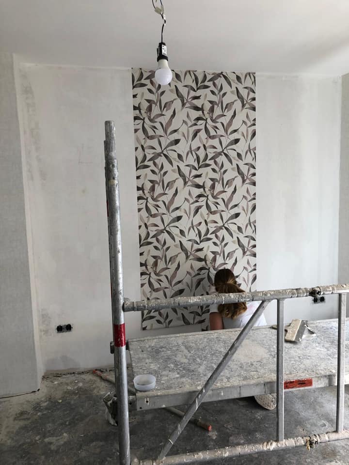 Rollgerüst vor der Wand, an der die Tapete mit Blattmuster angebracht wird.