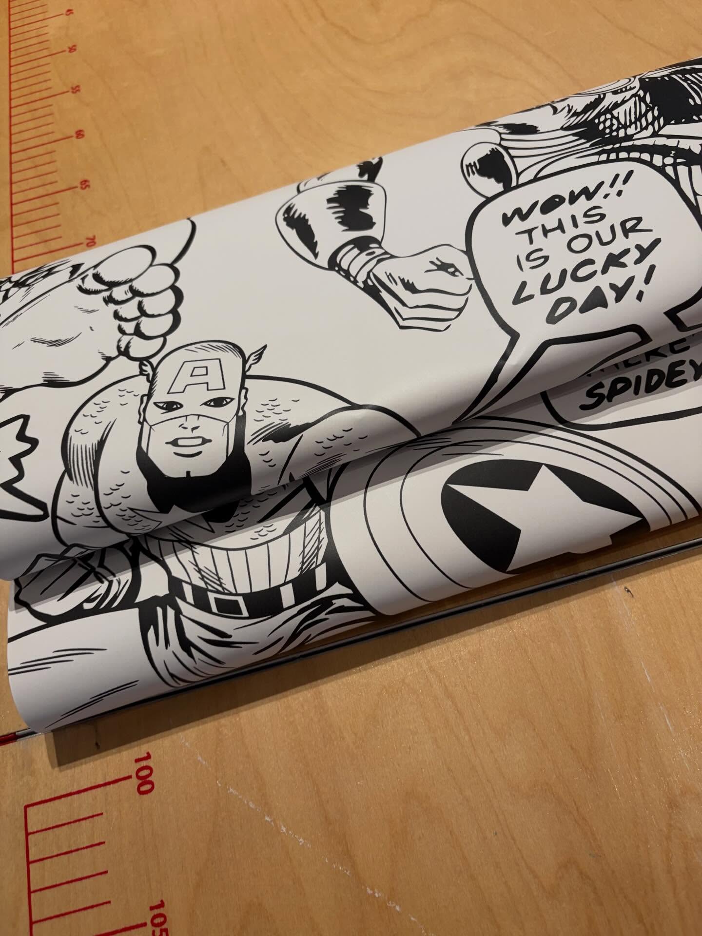 Tapetenbahn mit Comic-Motiv auf einem Tapeziertisch mit Maßskala.