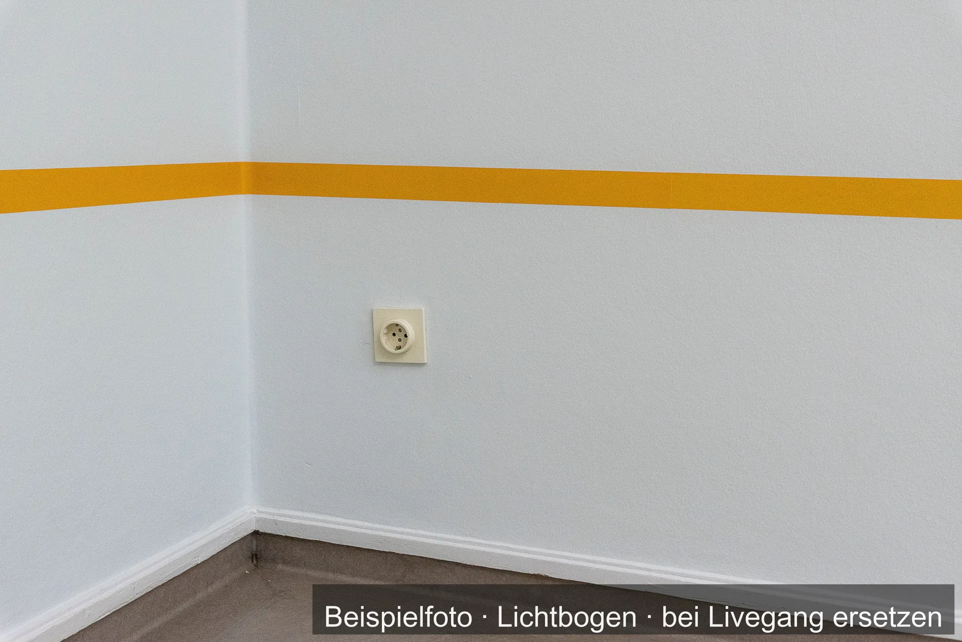 Hell gestrichener Raum mit einem gelben Farbstreifen an der Wand und einer Steckdose über der Fußleiste.